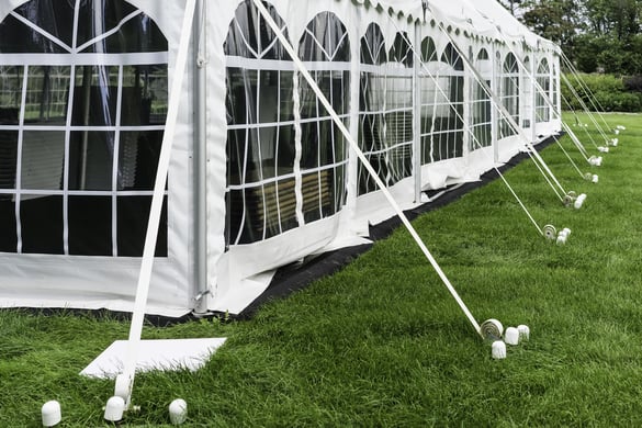 Corner and side of large white event tent with plastic windows, anchored on garden lawn in summer